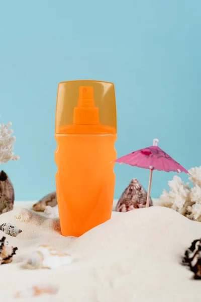 Orange spray bottle of sunblock near seashells on sand isolated on blue — Fotografia de Stock