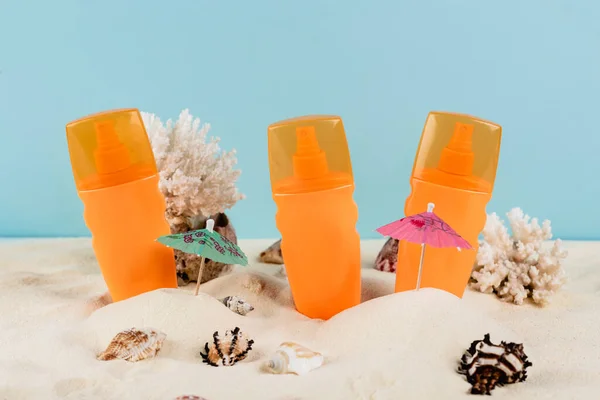 Botellas naranjas de bloqueador solar cerca de conchas marinas en arena aislada en azul - foto de stock