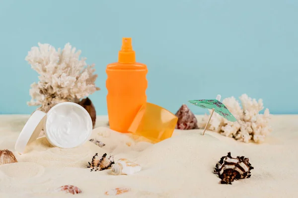 Crème cosmétique et bouteille de crème solaire près des coquillages sur sable isolé sur bleu — Photo de stock