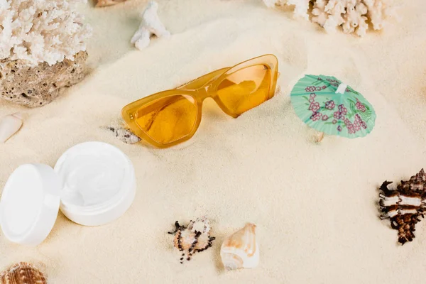 Top view of cosmetic cream near orange sunglasses and seashells on sand — Fotografia de Stock