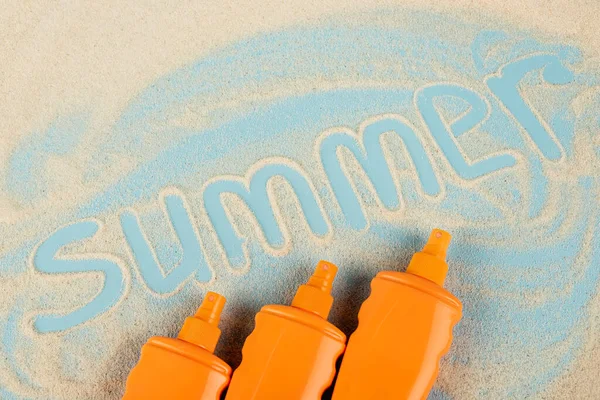Top view of orange bottles with sunblock near summer lettering on sand and blue surface — Fotografia de Stock