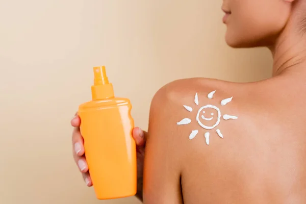 Vista ritagliata della donna con immagine di sole sorridente sulla spalla che tiene la protezione solare isolata sul beige — Foto stock