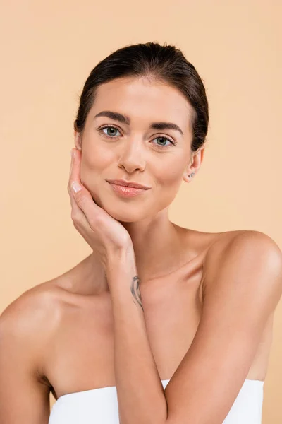 Sensual woman with naked shoulders touching face while posing isolated on beige, beauty concept — Fotografia de Stock