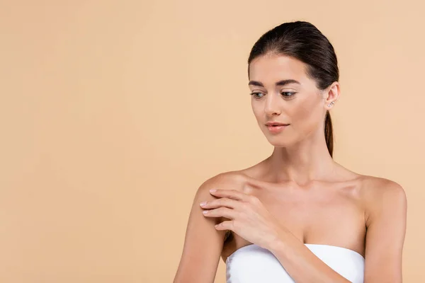 Mujer joven con la piel limpia tocando hombro desnudo aislado en beige, concepto de belleza — Stock Photo