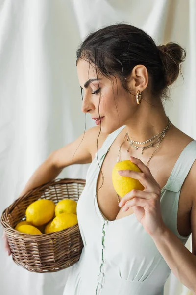 Mulher bonita no vestido segurando cesta de vime e limão no branco — Fotografia de Stock