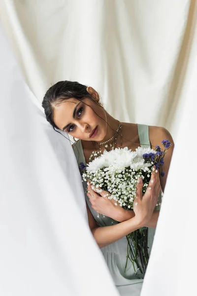 Hübsche Frau blickt in die Kamera, während sie Blumen auf weiß hält — Stockfoto