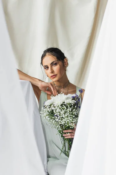 Брюнетка жінка дивиться на камеру, тримаючи квіти на білому — стокове фото
