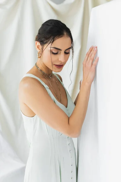 Morena mujer en vestido mirando hacia abajo mientras posando en blanco - foto de stock