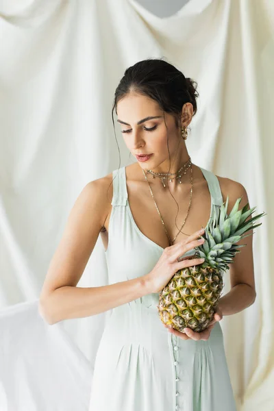 Brunette woman in dress posing with pineapple on white — Stock Photo