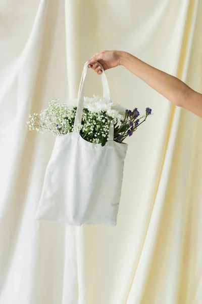 Cropped view of woman holding fabric shopper bag with flowers on white — Stock Photo