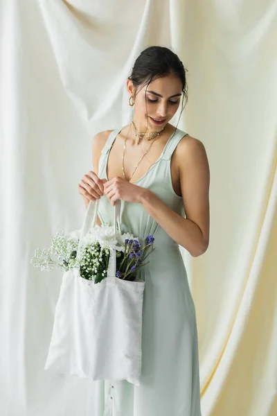 Mujer feliz sosteniendo bolso de comprador de tela con flores en blanco - foto de stock
