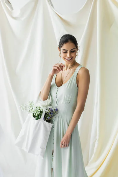 Mujer alegre sosteniendo bolso de comprador de tela con flores en blanco - foto de stock