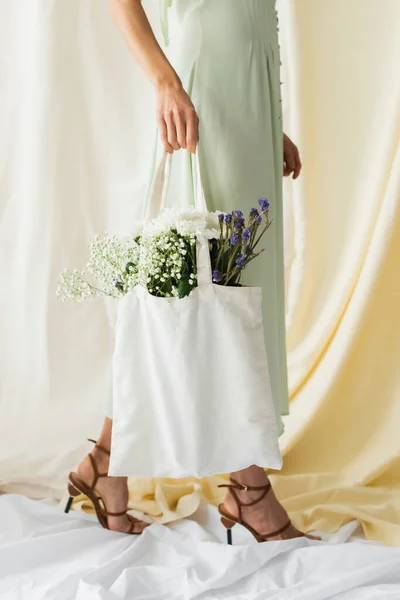 Vista ritagliata della donna che tiene borsa shopper tessuto con fiori e camminare su bianco — Foto stock