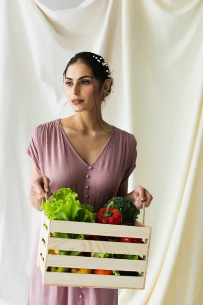 Brunette femme tenant boîte en bois avec des légumes sur blanc — Photo de stock