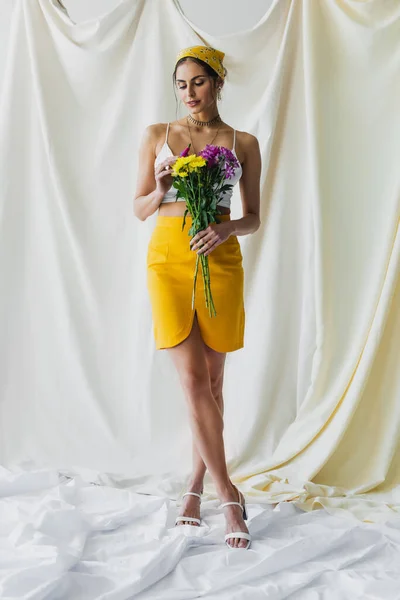 Повна довжина жінки в жовтому хустці, що тримає квіти на білому — стокове фото