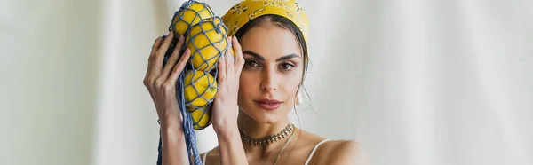 Woman in yellow headscarf holding string bag with lemons on white, banner — Stock Photo