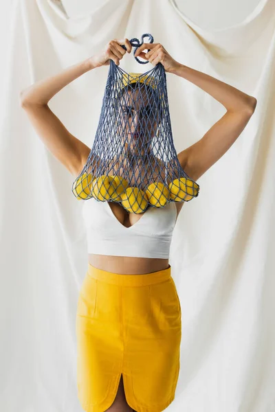 Woman in crop top holding string bag with lemons on white — Stock Photo