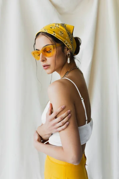 Mulher em óculos de sol amarelos e lenço de cabeça posando no branco — Fotografia de Stock