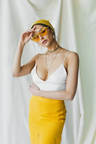 Mulher elegante em óculos de sol e lenço amarelo posando no branco — Fotografia de Stock