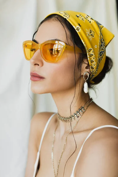 Mulher elegante em óculos de sol na moda e lenço de cabeça amarelo posando no branco — Fotografia de Stock