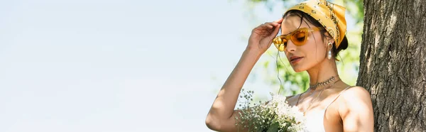 Femme élégante en lunettes de soleil et foulard jaune tenant des fleurs, bannière — Photo de stock