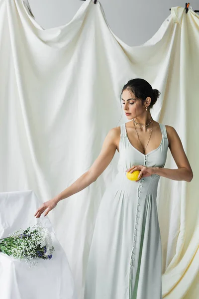 Jolie femme atteignant des fleurs tout en tenant citron frais sur blanc — Photo de stock