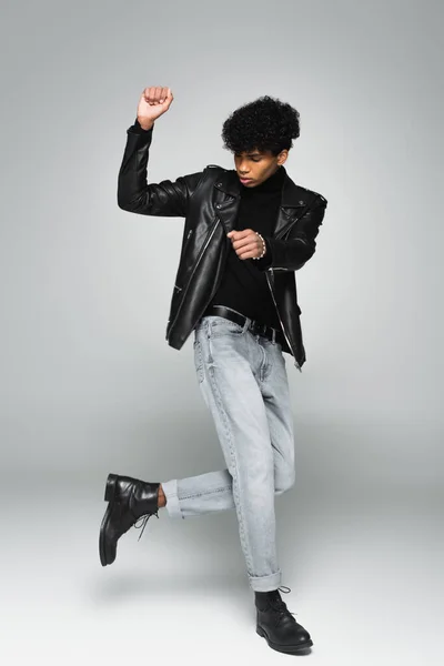 African american man in jeans, black leather jacket and boots dancing on grey background — Stock Photo