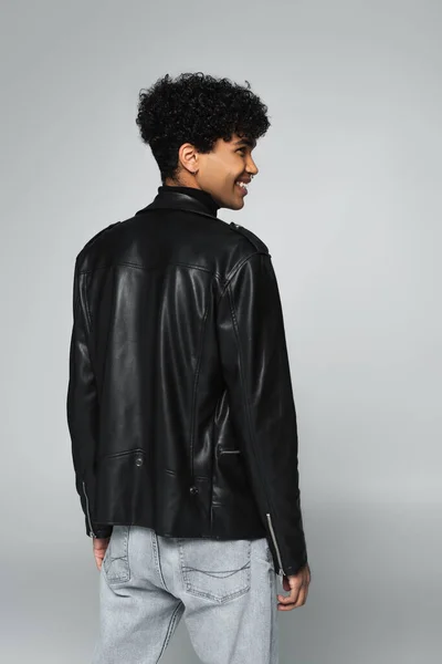 Щасливий афроамериканський чоловік в чорній шкіряній куртці посміхається ізольовано на сірому — стокове фото