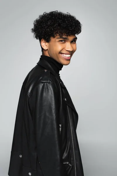 Happy african american man in black leather jacket smiling at camera isolated on grey — Fotografia de Stock