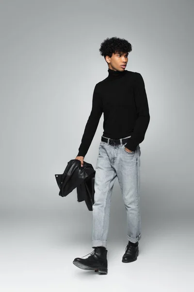 Trendiger afrikanisch-amerikanischer Mann, der mit der Hand in der Jeanstasche auf grauem Hintergrund geht — Stockfoto