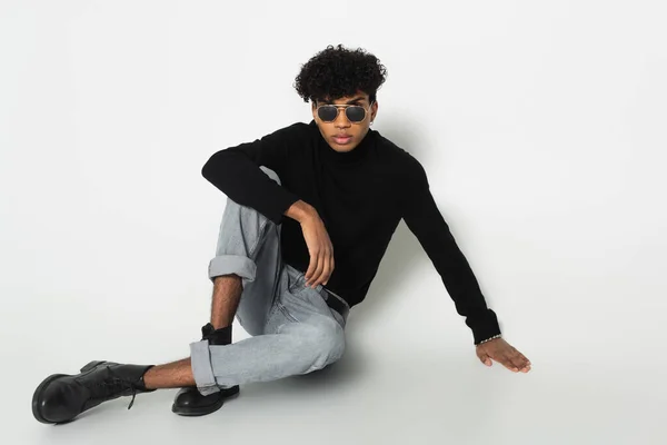 Young african american man in trendy clothes looking at camera while sitting on white background — Foto stock