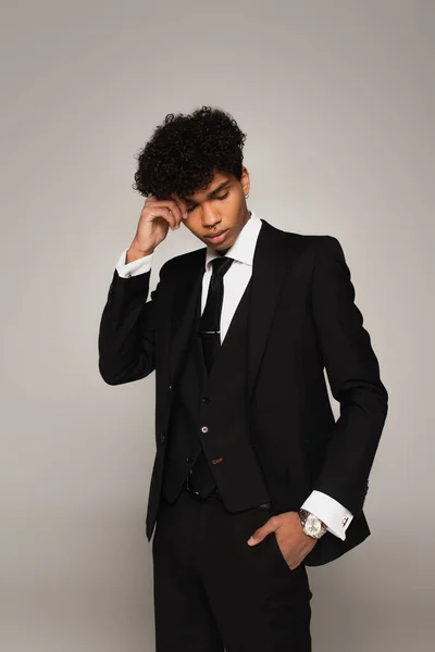 Trendy african american man in elegant suit posing with hand near head isolated on grey — Fotografia de Stock