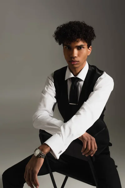 Афроамериканський бізнесмен в елегантному одязі, який дивиться на камеру, сидячи на сірому — стокове фото