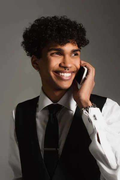 Trendy african american man smiling while talking on mobile phone isolated on grey — Stock Photo