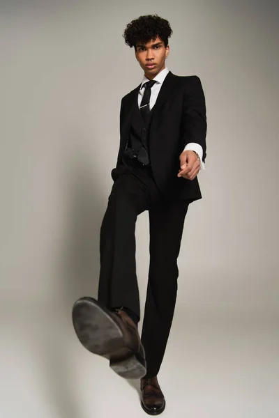 Low angle view of african american man in formal wear looking at camera while walking on grey — Stock Photo