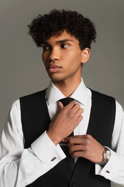 Элегантный африканский американец, регулирующий черный галстук, отводя взгляд на серый — стоковое фото