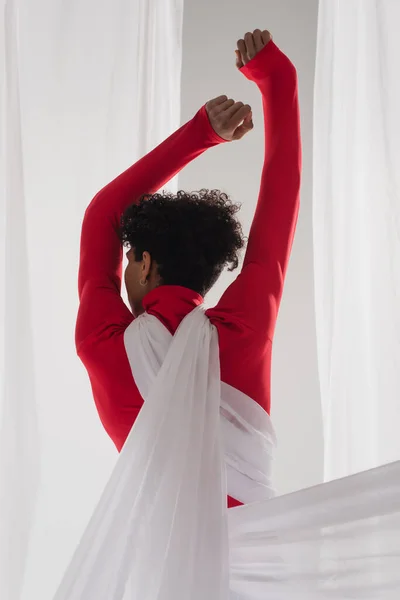 Back view of african american man, wrapped in white chiffon cloth, posing with raised hands — Stock Photo