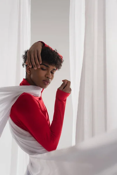 Stylish african american man posing in red turtleneck near white drapery — Stock Photo