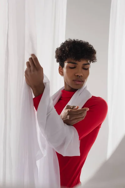 Кучерявий афроамериканський чоловік у червоній тканині черепашки позує біля білої тканини шифону — стокове фото