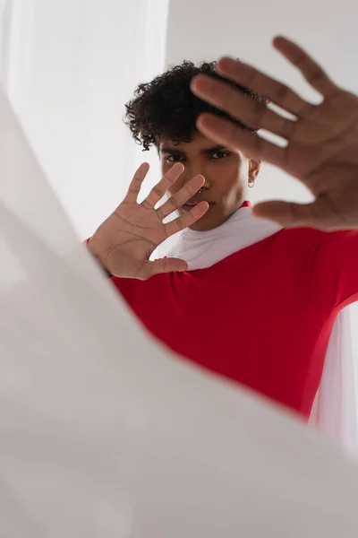 Young african american man in red turtleneck showing stop gesture near white blurred cloth — Foto stock