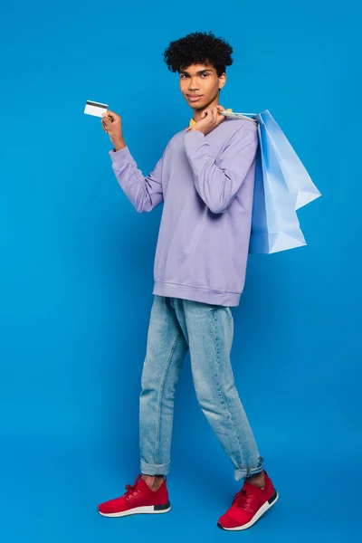 Full length view of african american man standing with shopping bags and credit card on blue background — Fotografia de Stock