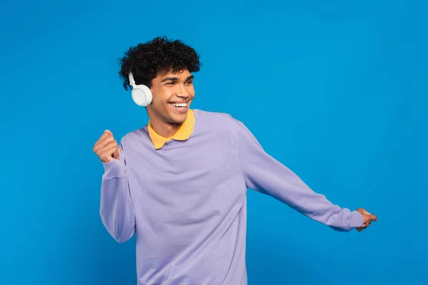 Excited african american man dancing in wireless headphones isolated on blue — Foto stock