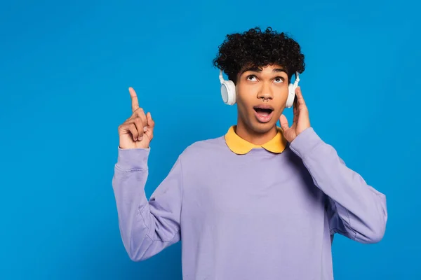 Surprised african american man in headphones pointing up with finger isolated on blue — Foto stock