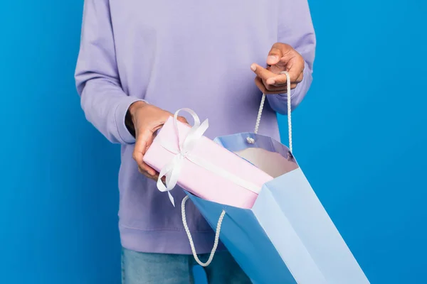 Cropped view of african american man with paper bag and gift box isolated on blue — Photo de stock