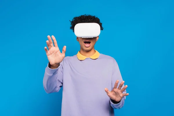 Amazed african american man in violet pullover gaming in vr headset isolated on blue — Foto stock