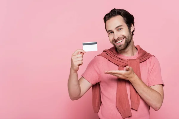 Улыбающийся мужчина указывает на кредитную карту, изолированную на розовый — стоковое фото