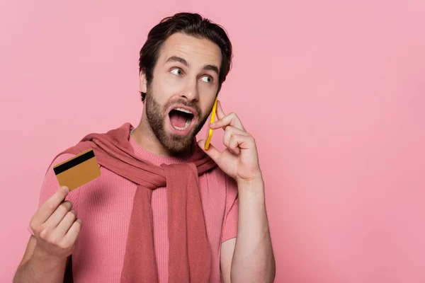 Verblüffter Mann telefoniert mit Handy und hält Kreditkarte isoliert auf rosa — Stockfoto