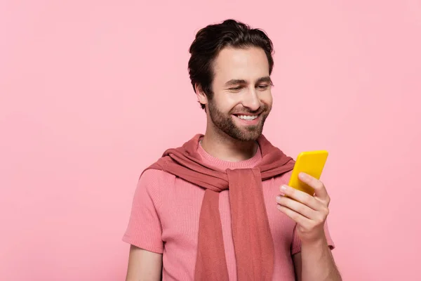 Brunette man smiling while using smartphone isolated on pink — Stock Photo