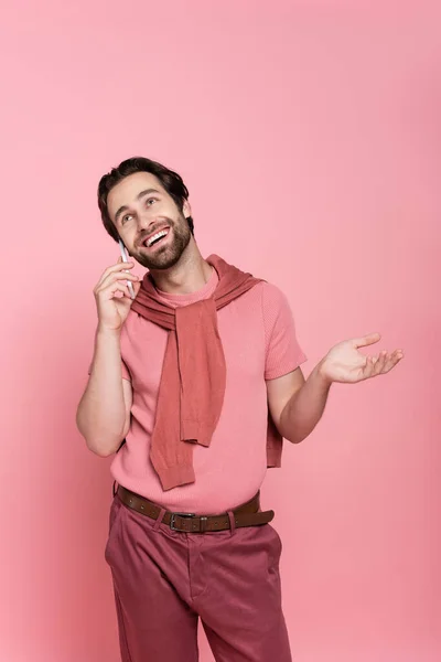 Uomo positivo guardando in alto mentre parla su smartphone isolato su rosa — Foto stock