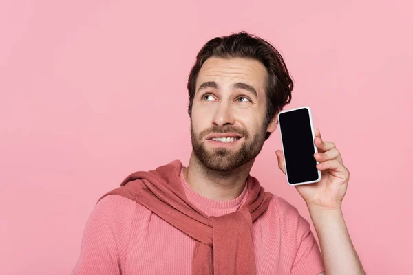 Hombre confundido sosteniendo teléfono inteligente con pantalla en blanco cerca de la oreja aislado en rosa - foto de stock